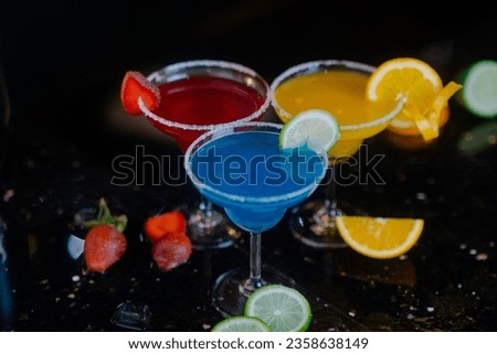 Bright glowing cocktails reflecting on glass, against a black background.