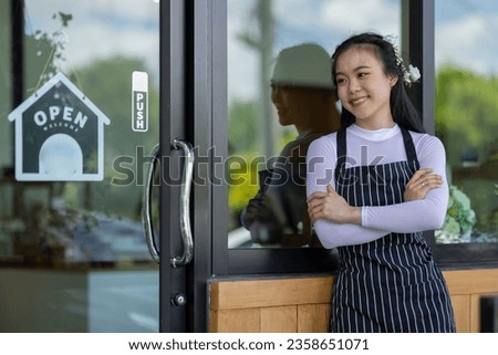 Portrait of asian smiling owner standing at her restaurant gate with open signboard. Young entrepreneur leaning at the cafeteria door, Chef or waiter standing in front of coffee shop.