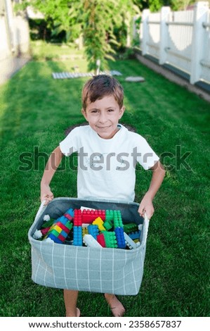Boy holding box full of plastic colorful blocks in garden sunset
