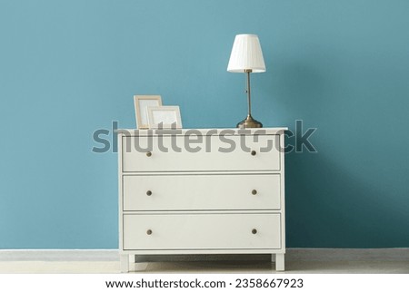 Blank picture frames and lamp on chest of drawers near color wall