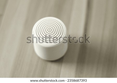 A white mini wireless speaker o a wooden floor and selective focus and shadows on right
