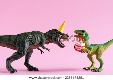 Cute happy green dinosaurs in birthday hats holding cake with flaming candles on pastel pink background. Copy space. Minimal art birthday card idea. Royalty-Free Stock Photo #2358695251