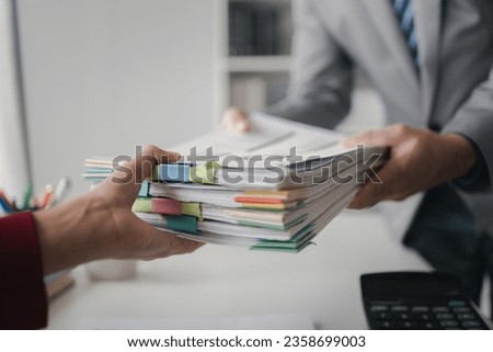 Two company employees handing over papers to each other, marketing staff handing over marketing analysis papers to department heads for presentation. Marketing analysis and planning concepts. Royalty-Free Stock Photo #2358699003