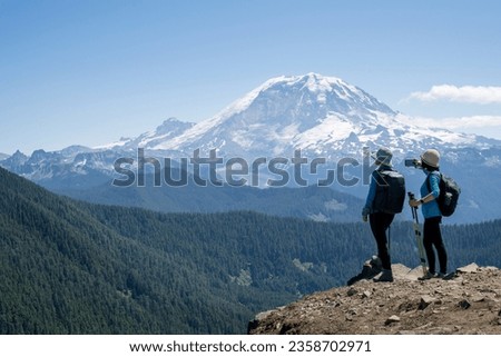 Two women enjoying the views on the Summit Lake trail. Taking smartphone photos of snow-capped Mount Rainier. Mt Rainier National Park. Washington State.   Royalty-Free Stock Photo #2358702971
