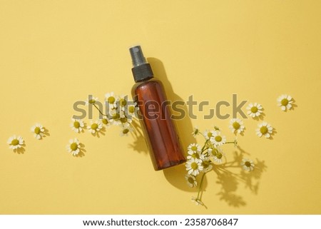 Against yellow background, some flowers and a pump bottle are featured. Top view. Branding mockup with Chamomilla (Matricaria chamomilla) extract