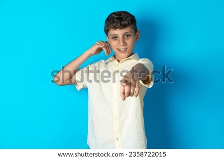 beautiful kid boy wearing casual T-shirt smiling cheerfully and pointing to camera while making a call you later gesture, talking on phone