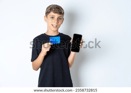 Photo of adorable beautiful kid boy wearing casual black T-shirt holding credit card and Smartphone. Reserved for online purchases
