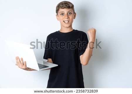 beautiful kid boy wearing casual black T-shirt hold computer open mouth rise fist