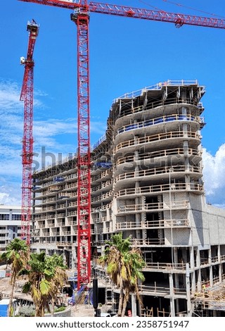 Vertical photo of a luxury hotel under construction with giant commercial cranes in the foreground.