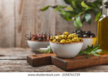 Green, black and red olives, olive oil on a brown wooden background. Fresh juicy olives in a bowl and fresh olive leaves. Vegan. Olive fruits. Place for text. Copy space. Royalty-Free Stock Photo #2358761729