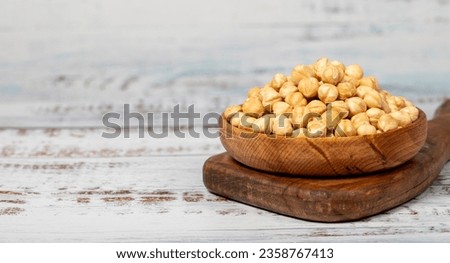 Roasted hazelnuts in wood bowl. Peeled hazelnuts kernel on white wood background. Copy space. Empty space for text Royalty-Free Stock Photo #2358767413