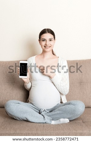 Pregnant woman showing smartphone with black screen in sofa.