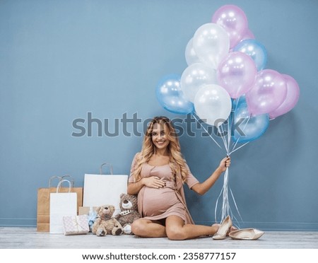 Beautiful pregnant woman holding balloons, looking at camera and smiling while sitting near her presents during baby shower Royalty-Free Stock Photo #2358777157