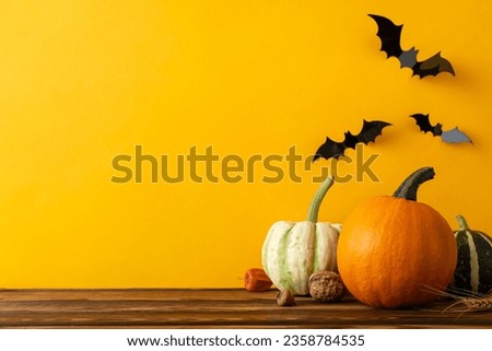 Halloween setup. Side view photo of pumpkins, ghostly gourds, walnut, physalis, acorn on wooden table, with hauntingly orange wall background, decorated with eerie bats, space for your spooky message