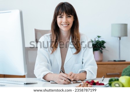 Shot of beautiful smart nutritionist woman working with computer while looking at camera in the nutritionist consultation Royalty-Free Stock Photo #2358787199