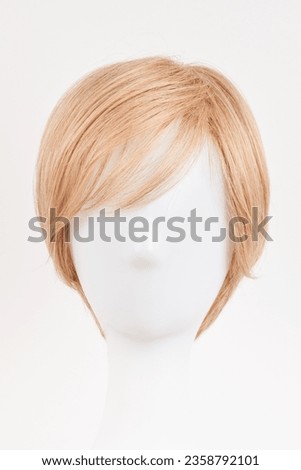 Natural looking blonde fair wig on white mannequin head. Short hair cut on the plastic wig holder isolated on white background, front view
