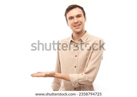 Portrait of young caucasian man holding something in hand, demonstrating product, smiling joyfully isolated on white studio background with copy space
