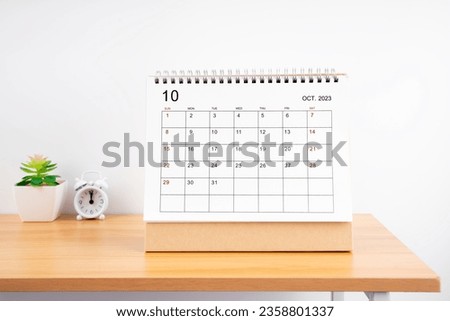 October Monthly desk calendar for 2023 year and alarm clock on wooden table.