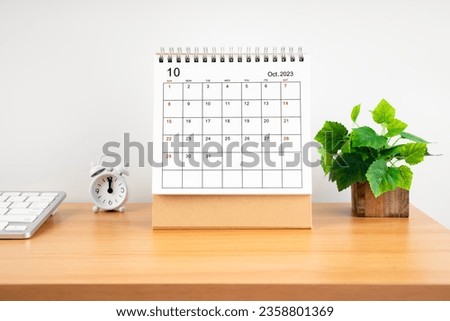 October 2023, Monthly desk calendar for 2023 year on wooden table with alarm clock.
