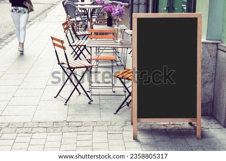 Blank restaurant blackboard on the street with blurry woman pedestrian passing by