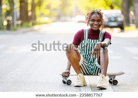 Portrait of a black non-binary person with a skateboard sitting on the street
