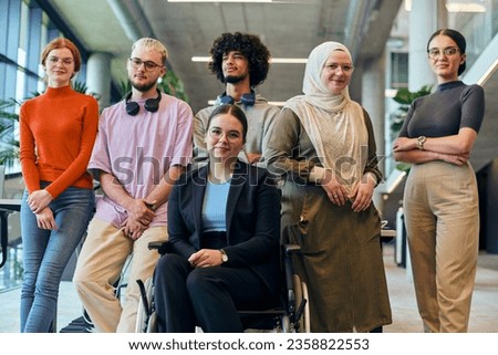 In a spacious and modern startup office, a diverse group of business colleagues, including a colleague in a wheelchair, collaborates and interacts, exemplifying inclusivity, diversity, and teamwork in Royalty-Free Stock Photo #2358822553