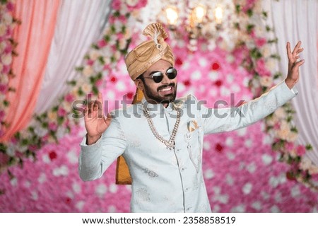 Young man or Groom with Funky Eyeglasses dancing on wedding stage on decorated background - concept of Joyful Celebration, Excitement and marriage ceremony. Royalty-Free Stock Photo #2358858519