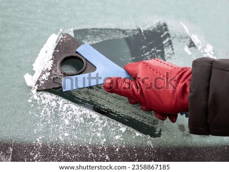 Picture of a hand holding window scraper and removing ice of the car window