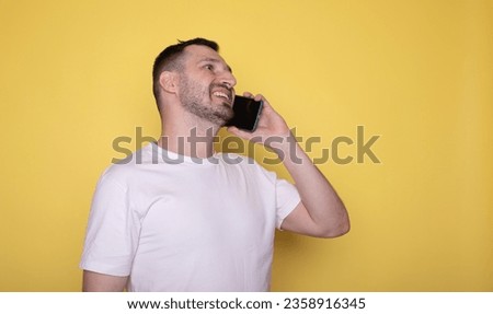  Young man talking by cell phone and smiling, yellow background, copy space