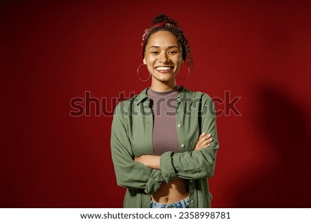 Portrait of charming smiling woman looks camera with crossed hands on red studio background