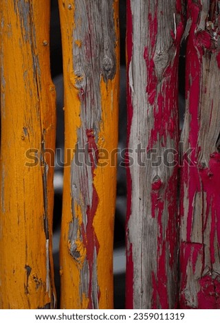wooden fence posts close together painted yellow and red with paint peeling allowing wood grain showing underneath  layer of paint vertical image room for type colorful background backdrop  wallpaper Royalty-Free Stock Photo #2359011319