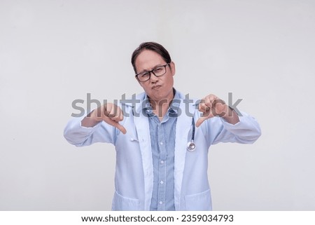 An unimpressed and dismissive doctor gives the double thumbs down sign. Of asian descent, middle aged male in his 40s. Isolated on a white background. Royalty-Free Stock Photo #2359034793