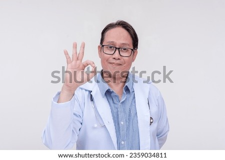 A supportive family doctor makes a reassuring gesture, making the ok sign. Giving his approval. Of asian descent, middle aged male in his 40s. Isolated on a white background.