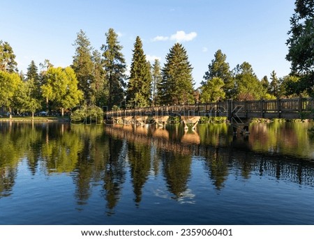 Beautiful and tranquil lush wide angle view of bridge over Mirror Pond in Drake Park, Bend, Oregon, on a blue sky sunny summer afternoon. Royalty-Free Stock Photo #2359060401