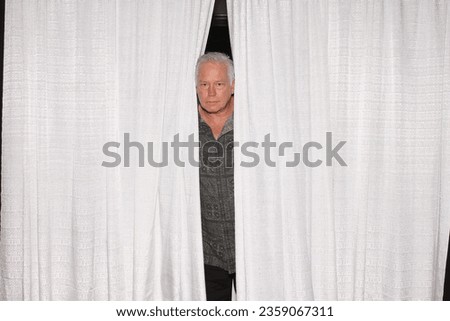 Photo Booth. A man peaks through white curtains while in a Photo Booth at a Wedding or Special Event. People around the World Love Photo Booths. Everyone gets their pictures taken and printed out. 