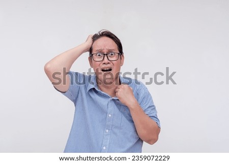 A panicked middle aged asian man grabbing his hair and the collar of his shirt buckling under the intense stress of work or personal issues. Isolated on a white backdrop. Royalty-Free Stock Photo #2359072229