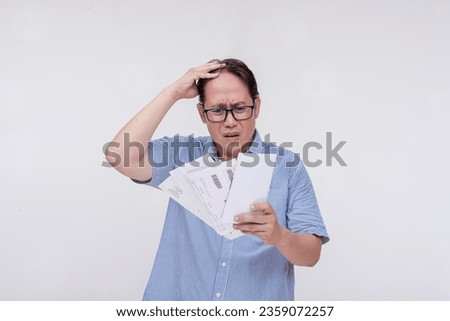 A worried middle aged asian man panics over multiple unpaid and past due bills. Isolated on a white backdrop. Royalty-Free Stock Photo #2359072257