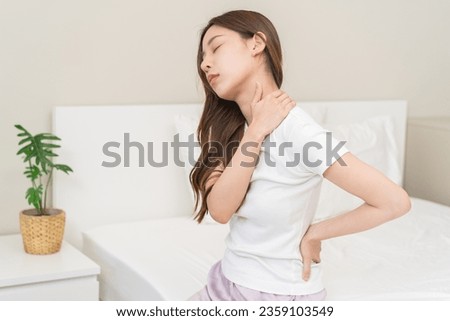 Pain body muscles stiff problem, asian young woman painful with back, neck ache from work hand holding massaging rubbing shoulder hurt, sore sitting on bed in room at home. Health care and medicine. Royalty-Free Stock Photo #2359103549