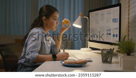 Asia people young girl work busy at home office sit on desk crave sweet junk fast food eat bite donut at night. Workforce issue bad habit stress relief by fat diet break time late dinner in hard job. Royalty-Free Stock Photo #2359115287