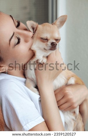 Middle aged lovely woman kissing her doggy Chihuahua in apartment indoors. Photo of funny Chihuahua dog in hands of adult lady at home. Concept of pet love and family friendship. Copy ad text space
