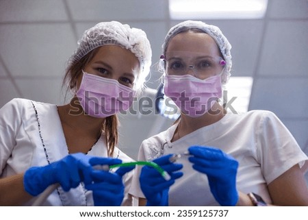 Women dentist doctor with assistant in pink medical masks holding equipment at dental office in medical clinic, bottom view, looking at camera. Medicine human dentistry concept. Copy ad text space