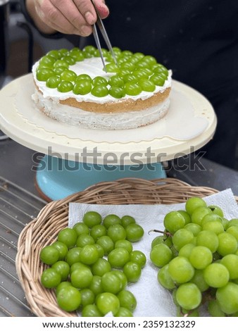 Woman holding plate with delicious Shine Muscat cream cake. 
Shine Muscat on a wooden basket. Fresh Shine Muscat topping with cream and yellow flower. Bakery picture free space for text.