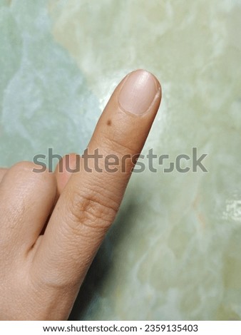 The index finger has a small black mole on the tip.  There is a green background of the table.