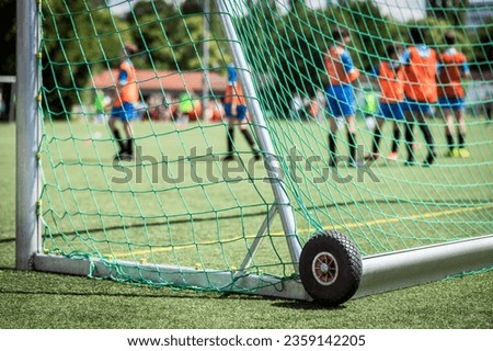 Soccer Goal Post with Net in focus. Mobile Soccer Goal Goalpost with Wheels on Football Field with Football Players Children. Sport Background and Equipment.  Royalty-Free Stock Photo #2359142205
