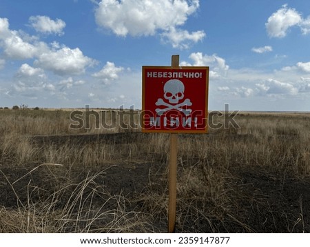 danger sign mine in Ukrainian near an agricultural field which in some places was scorched by explosions during the war in Ukraine, translation: "Mine danger"