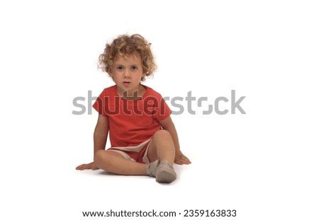 front view of a boy dressed in summer clothes sitting on group and looking at camera on white background (3 year old) Royalty-Free Stock Photo #2359163833