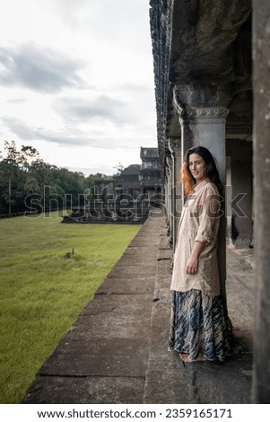 Young girl with long brown hair and long earth-coloured dress in the ruins of the Angkor temple