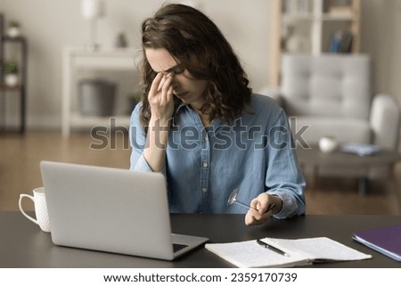 Tired frustrated freelance employee girl working at laptop, taking eyeglasses off, touching closed eyes, rubbing eyelids, nose, face, suffering from weak eyesight, itchy eyes, headache Royalty-Free Stock Photo #2359170739