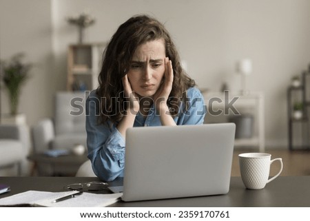 Sad gen Z freelancer girl suffering from headache at workplace, touching head at laptop, looking at screen with despair, frustration, getting problems with software, Internet connection Royalty-Free Stock Photo #2359170761