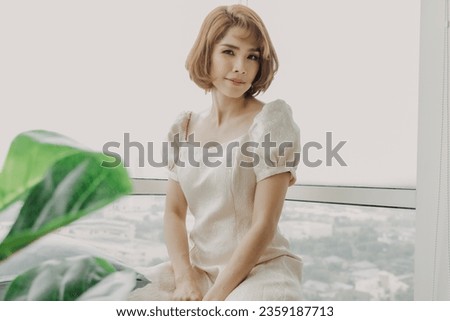 Soft and sweet looking Asian woman wears white dress and full makeup.